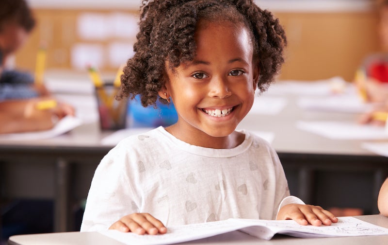 Child smiling while reading book in class.